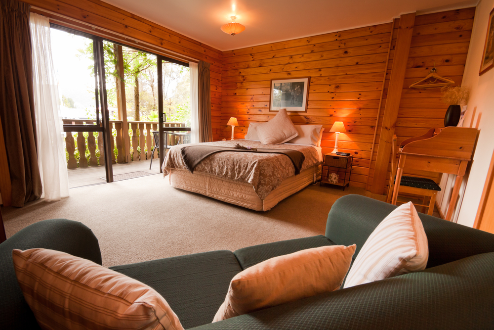 Wood panelled, cozy cabin bedroom with a sliding glass door and chair.