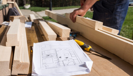 Close-up of a person putting together pieces of wood with a blueprint laying on top.