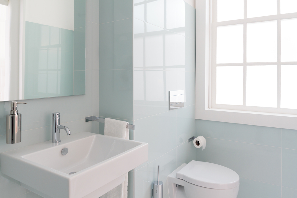 Light-coloured bathroom with light blue tiled walls and a window.