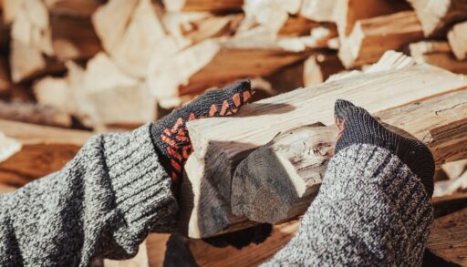 Man wearing black gloves stacking two pieces of firewood.