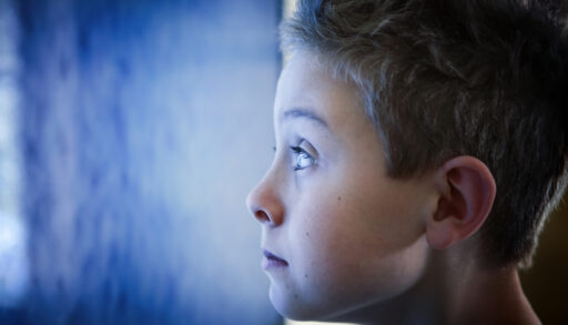 Close-up of a young boy staring at a blue television screen.