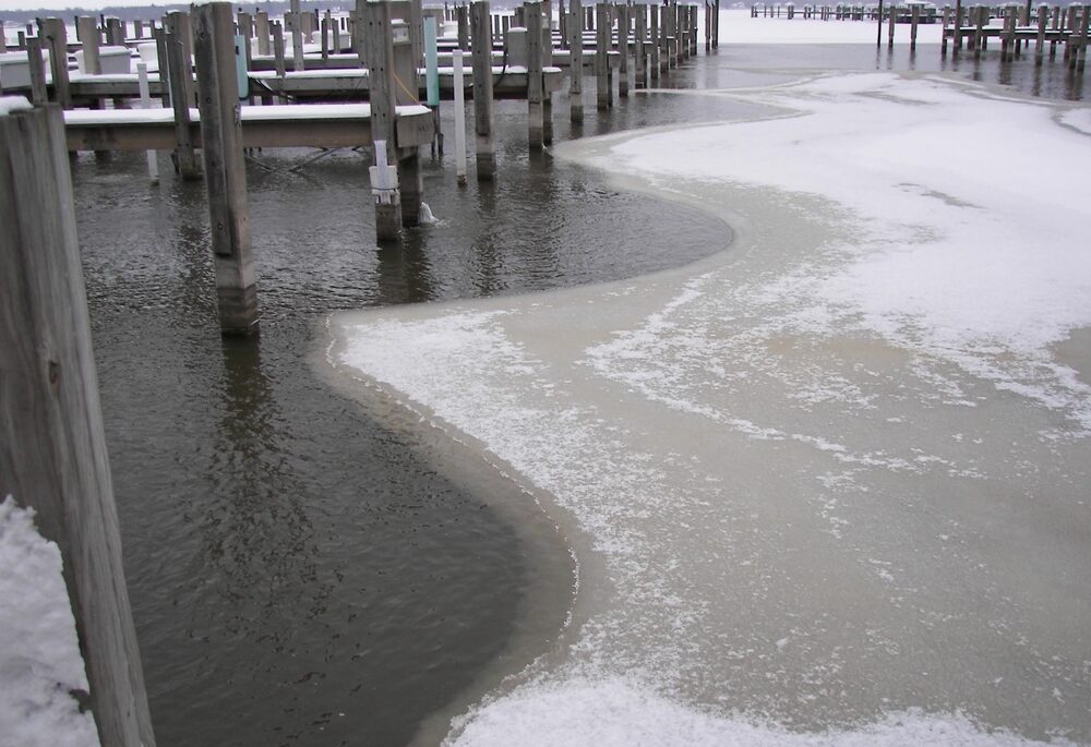 Ice on a lake underneath a row of dock piers.