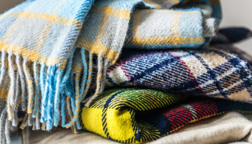 Stack of patterned, woollen blankets in shades of blue, yellow and red.