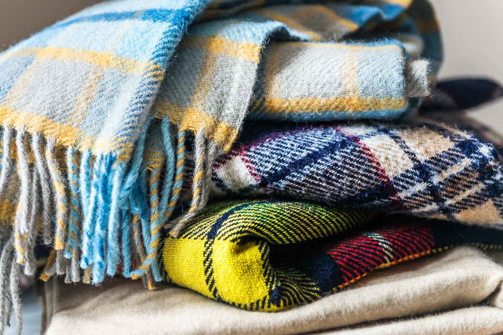 Stack of patterned, woollen blankets in shades of blue, yellow and red.