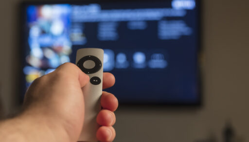 Person holding an Apple TV remote and pointing it at a television.