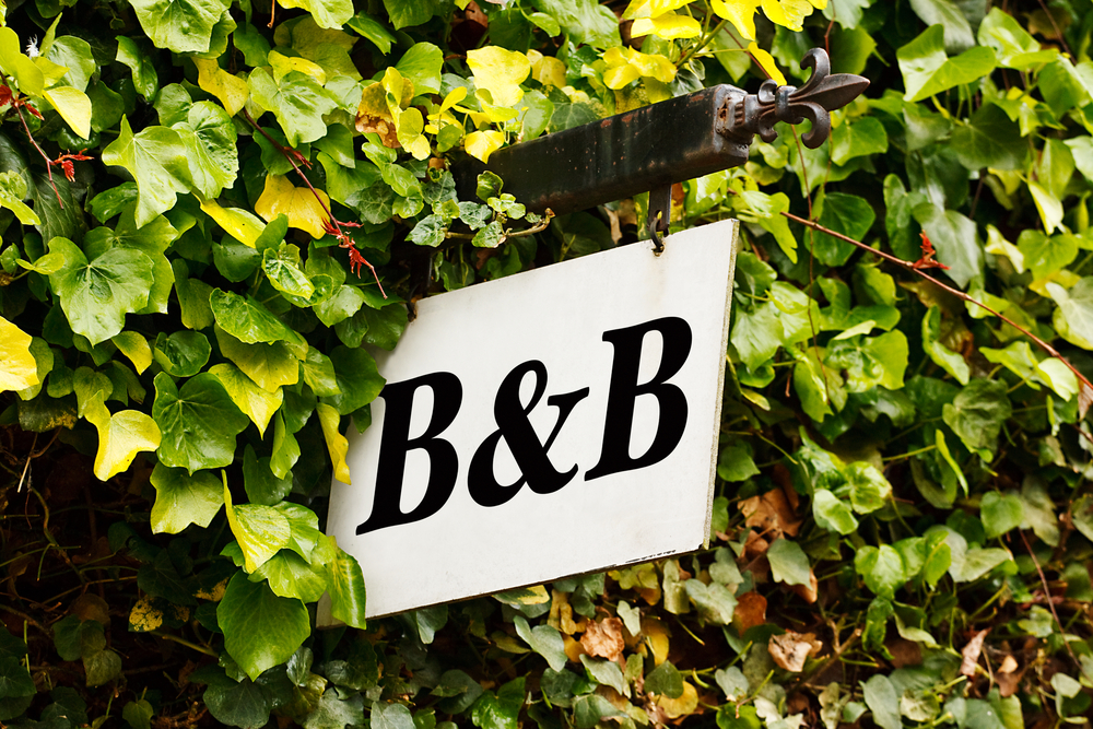 Black and white sign with "B&B" written on it and surrounded by a green hedge.