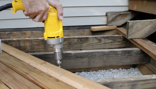Man using a yellow electric drill to build a deck.