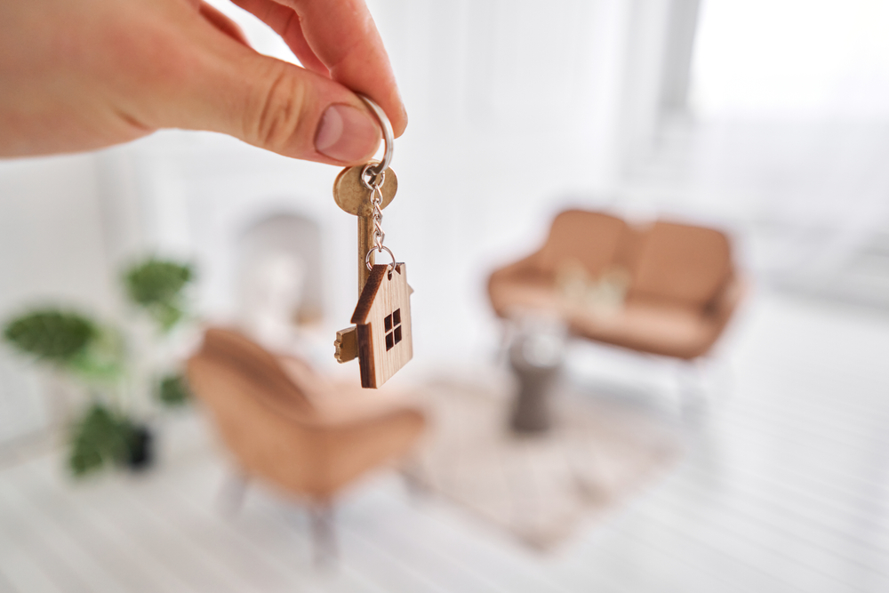 Person holding a house key with a wooden house keychain.