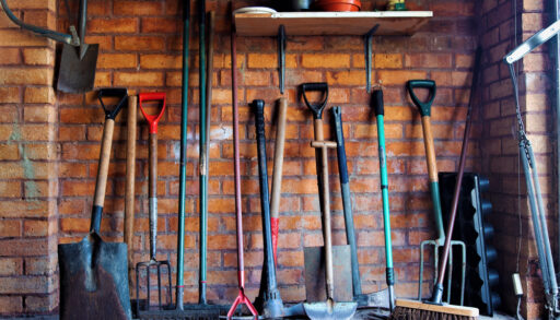 Interior of a brick tool shed with gardening tools lined up along the wall.