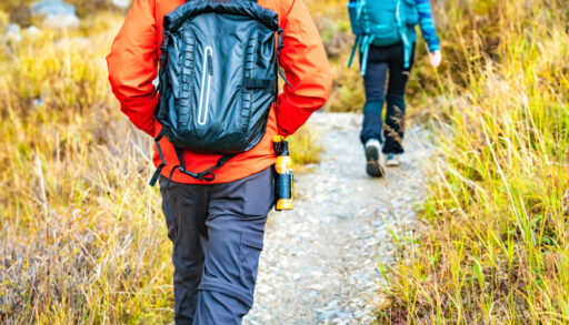 Two people, one wearing an orange jacket and one wearing a blue jacket, walking along a hiking trail.