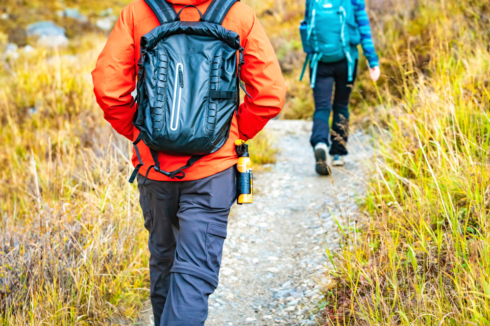 Two people, one wearing an orange jacket and one wearing a blue jacket, walking along a hiking trail.