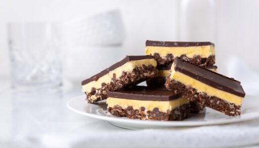 Plate of Nanaimo bars with white dishes in the background.