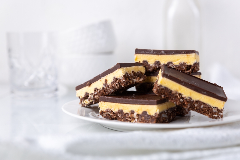 Plate of Nanaimo bars with white dishes in the background.