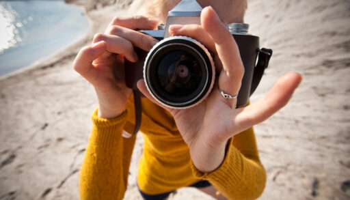 Woman in a yellow sweater holding an old camera and pointing it at the photographer.