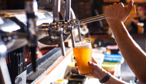 Bartender pouring a glass of amber-coloured beer from a tap.