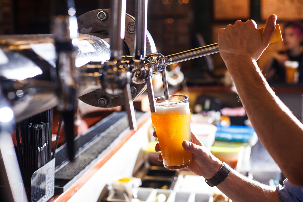 Bartender pouring a glass of amber-coloured beer from a tap.