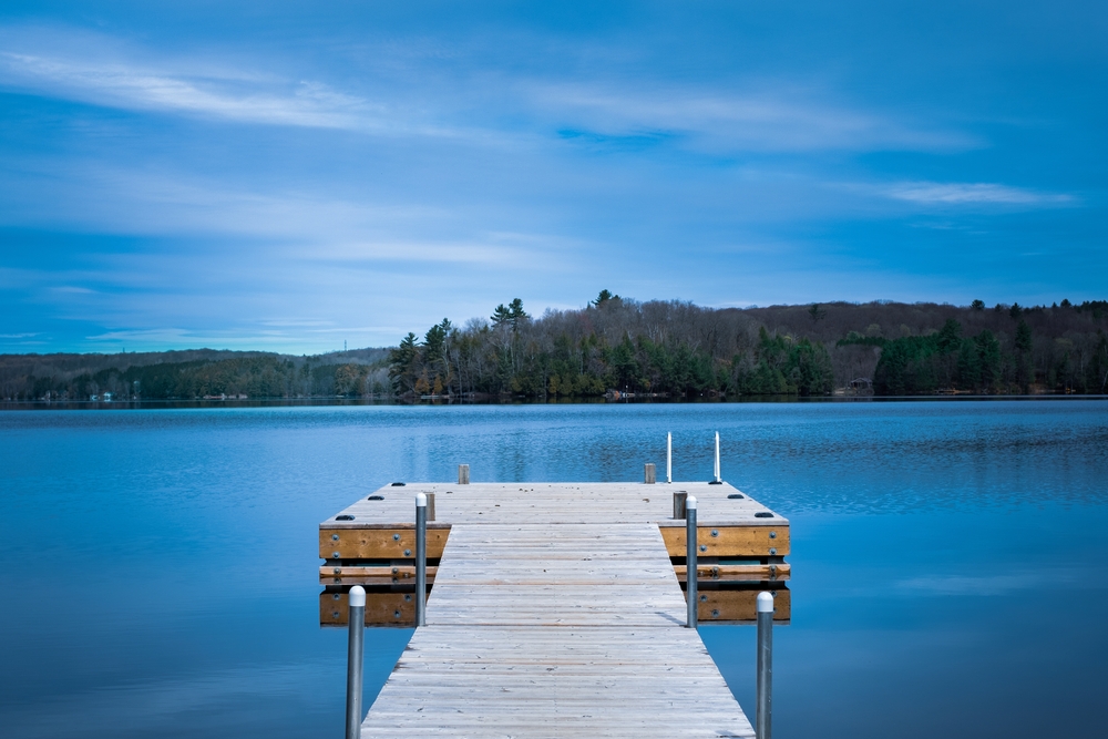 Wooden dock on a lake across from a shoreline covered with trees.