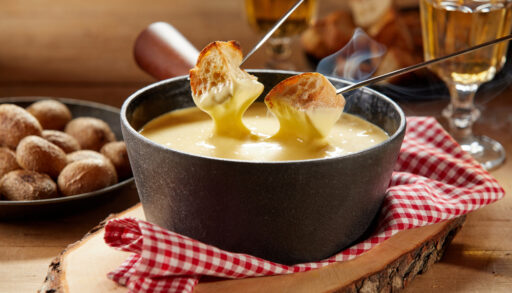 Close-up of bread being dipped in cheese fondue in a cast iron pot.