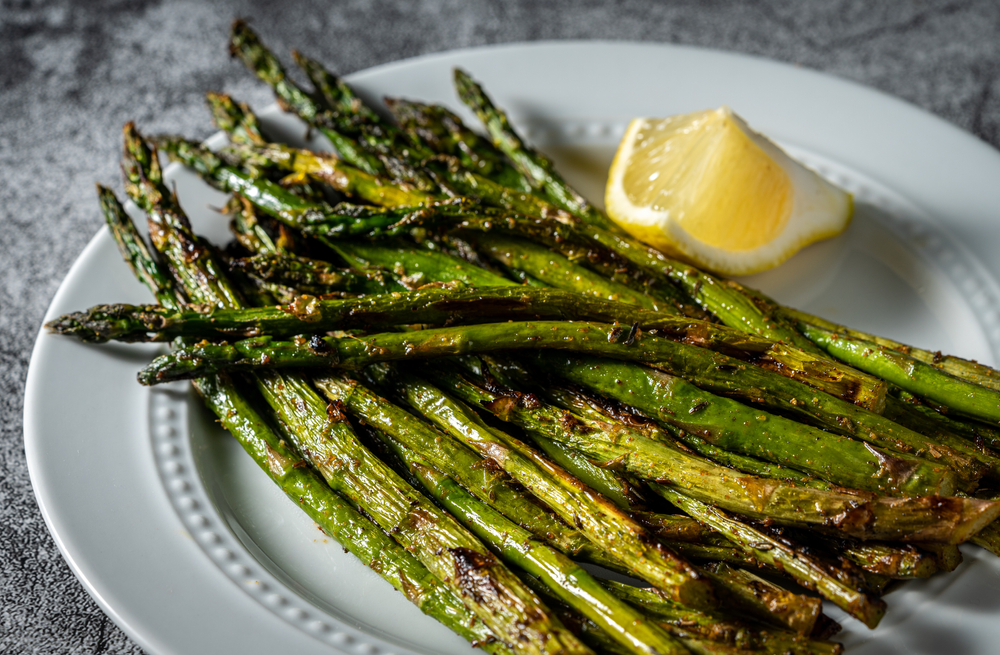 Close-up of grilled asparagus on a white serving plate with a lemon wedge.