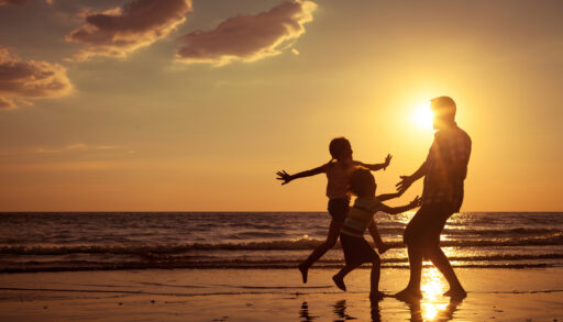 Silhouette of father and children playing on a beach at sunset.