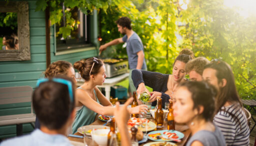 Group of people barbecuing and sitting on a patio drinking beer.