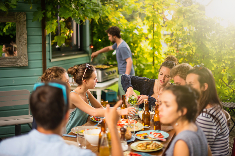 Group of people barbecuing and sitting on a patio drinking beer.