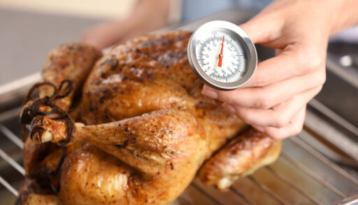 Close-up of a person using a meat thermometer to check the temperature of a cooked chicken.