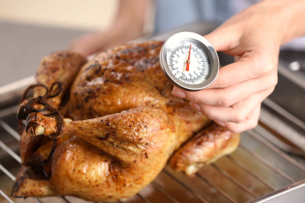 Close-up of a person using a meat thermometer to check the temperature of a cooked chicken.