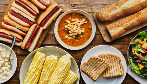 Overhead of a tabletop spread with soup, bread, corn on the cob and salad.