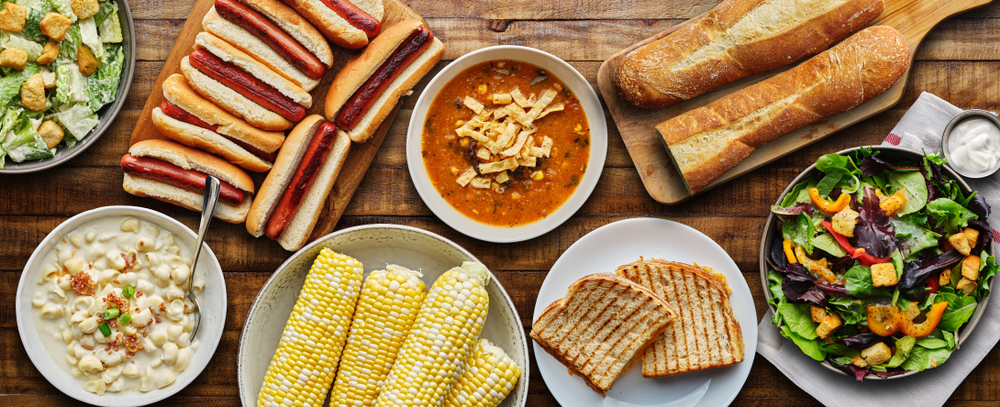Overhead of a tabletop spread with soup, bread, corn on the cob and salad.