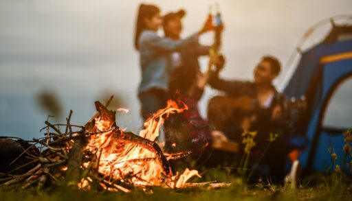 Close-up of a campfire with a tent and group of people in the background.