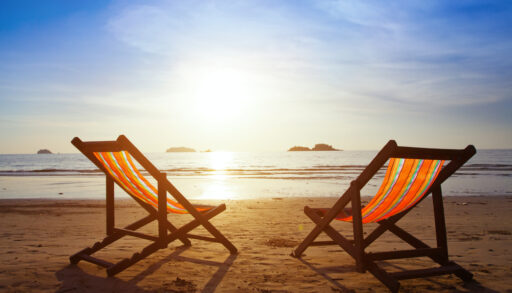 Two orange-striped folding beach chairs facing a sunset over the ocean.
