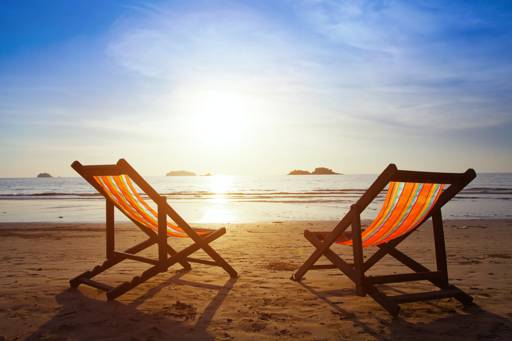 Two orange-striped folding beach chairs facing a sunset over the ocean.