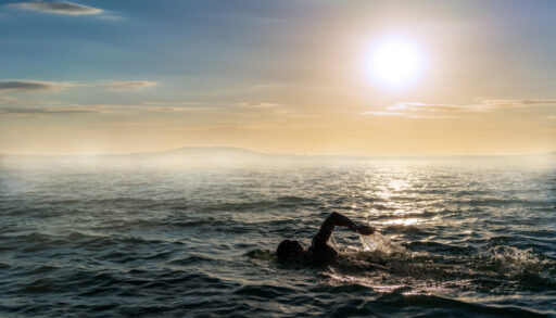 Silhouette of a man swimming in open water at sunset.