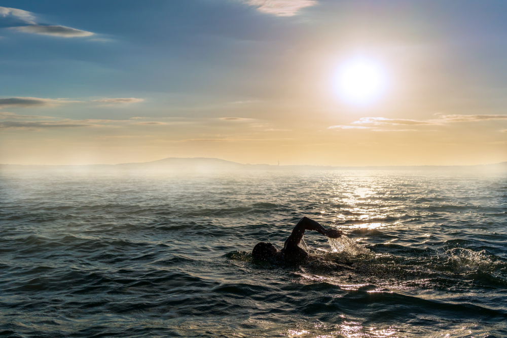 Silhouette of a man swimming in open water at sunset.