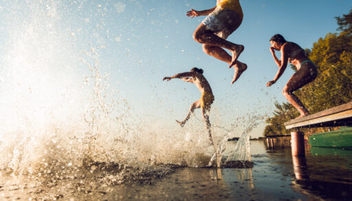Group of people jumping off a dock into a lake.
