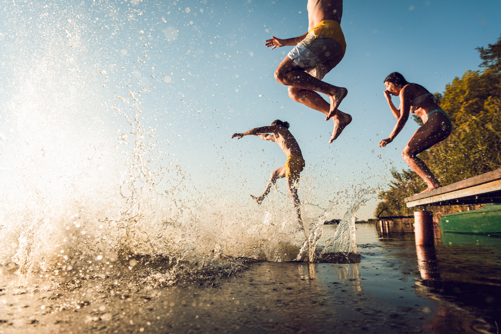 Group of people jumping off a dock into a lake.