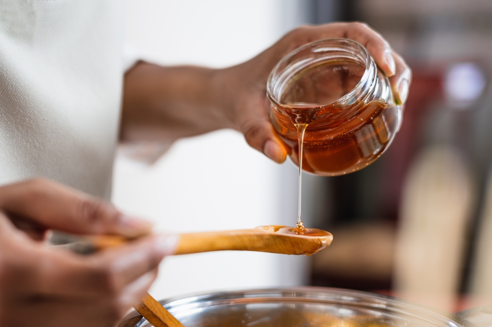 Close-up of a woman pouring honey from a jar onto a wooden spoon.