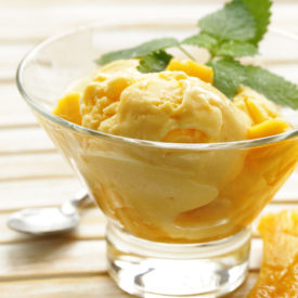 Light-orange-coloured mango ice cream, with basil leaves on top.