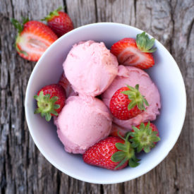 A bowl of strawberry ice cream topped with fresh strawberries.