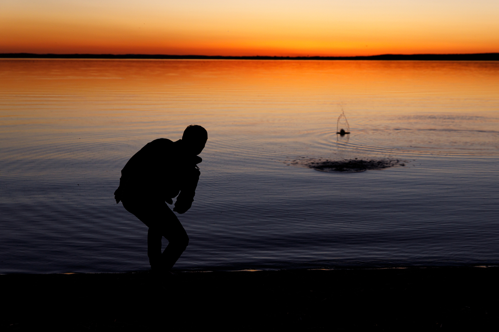 Silhouette of a man skipping stones on a lake at sunset.