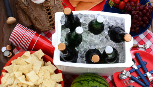 Overhead view of beer bottles in a red cooler surrounded by cups and chips.