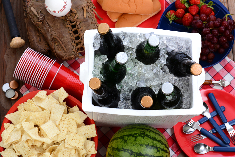 Overhead view of beer bottles in a red cooler surrounded by cups and chips.