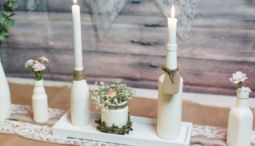Wine bottles painted white and repurposed as candlesticks for a wedding arrangement.