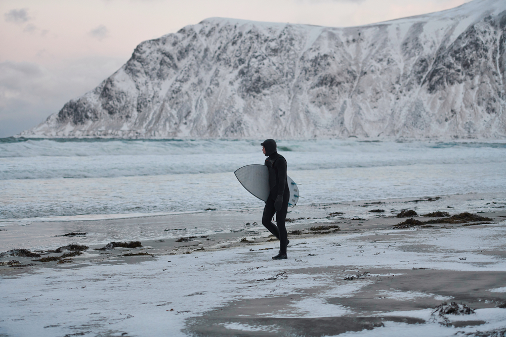 Cold water surfer carrying a surfboard and walking towards the Arctic ocean.