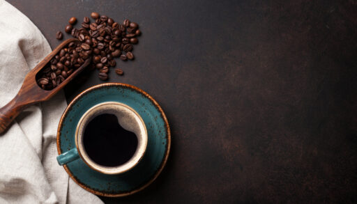 Overhead view of a teal coffee cup with a wooden scoop of coffee beans next to it.