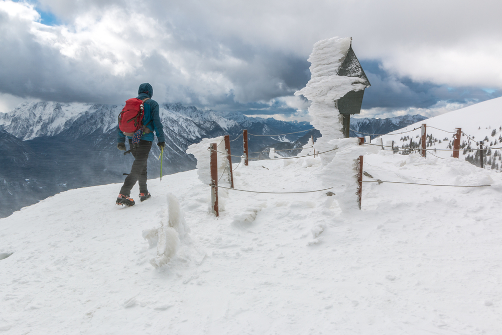 Mountaineer walking along a mountain in Slovenia with a post covered in rime ice.