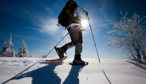 Low angle of a person wearing snowshoes and hiking in the snow, with the sun shining behind them.