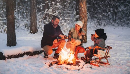 Parents and a child sitting around a winter campfire.