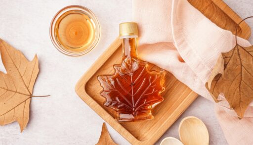Overhead view of a bottle of maple syrup on a wooden board next to a tea towel.